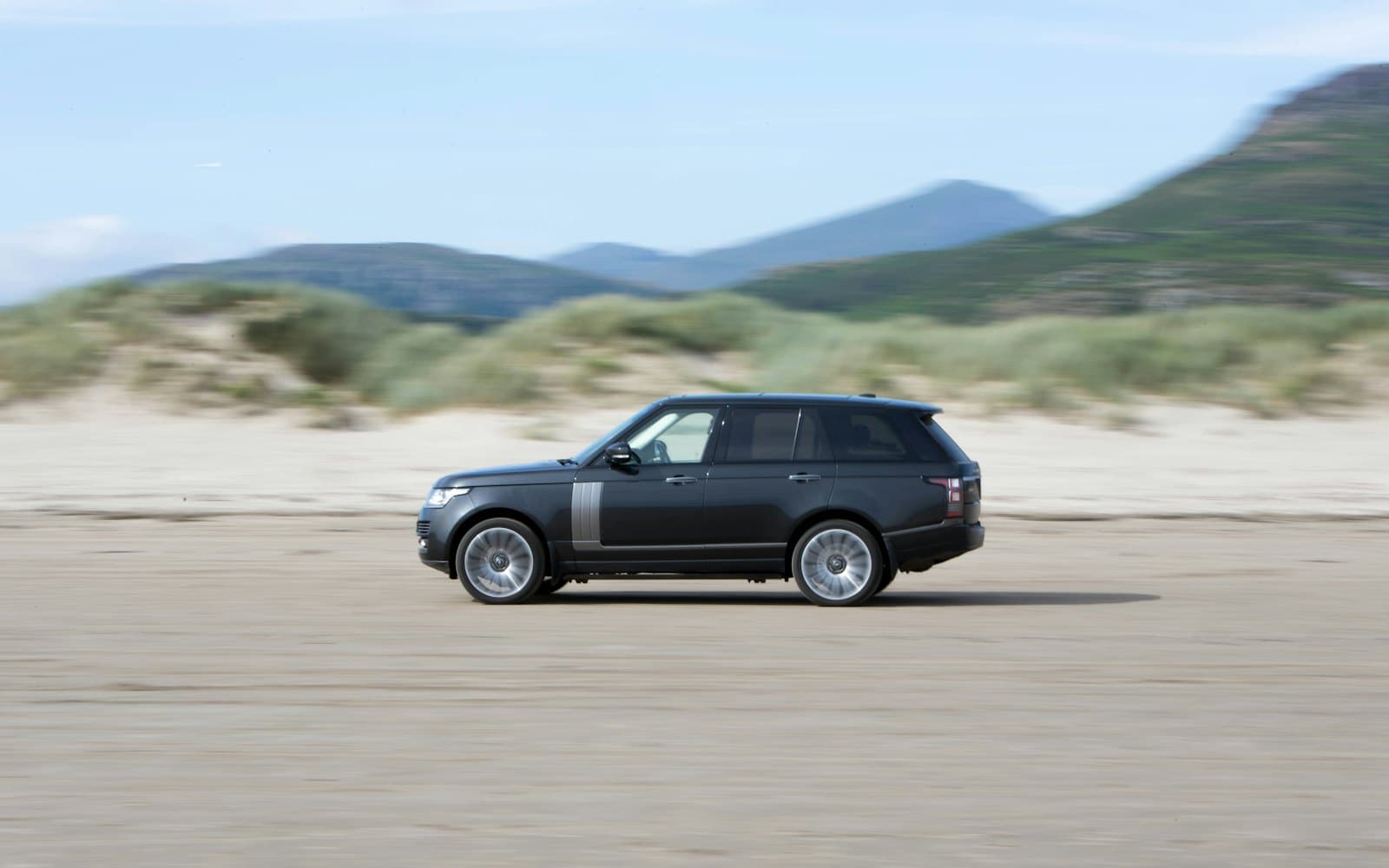 A dark Range Rover driving on a beach road